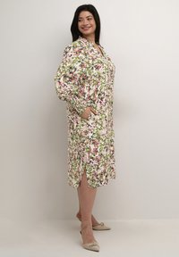 Bloemenprint jurk met lange mouwen, knopen en twee zijzakken. Kleuren zijn roze, groen en wit. Beschikt over een zijsplit voor bewegingsvrijheid.