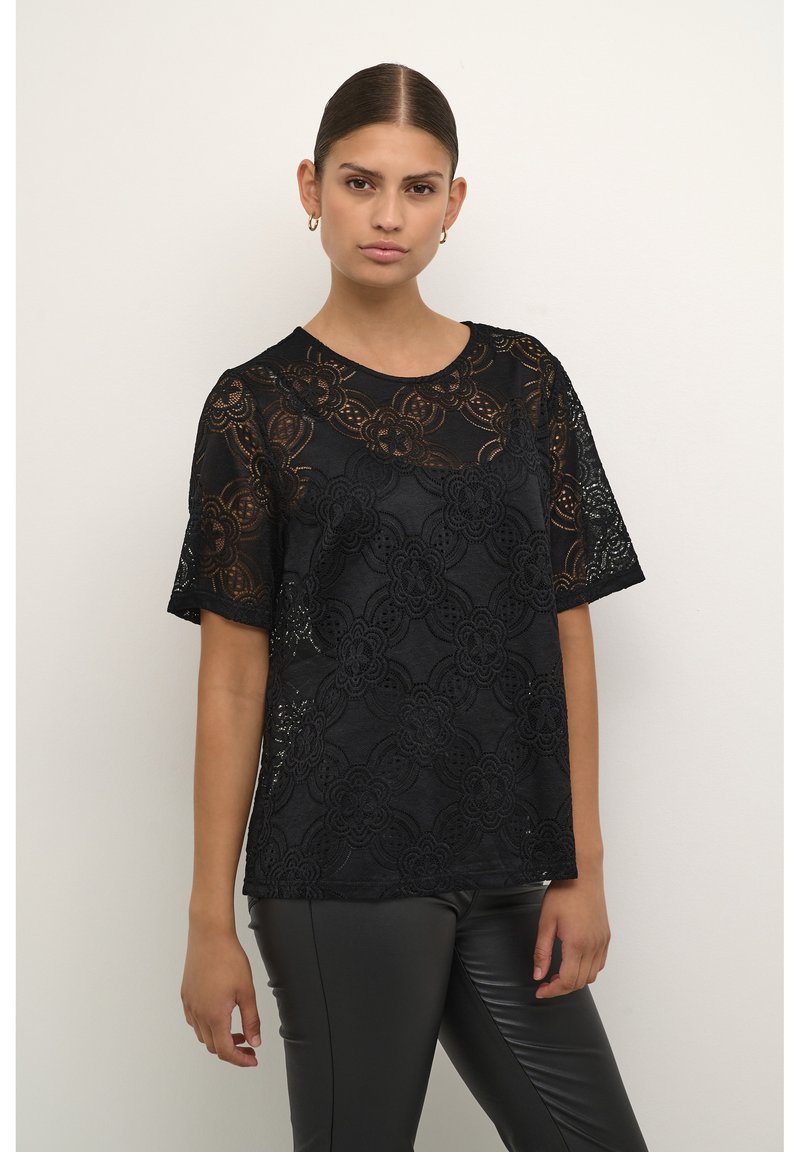 Schwarzes Spitzenoberteil mit Blumenmustern, kurzen Ärmeln und rundem Ausschnitt. Kombiniert mit glänzenden schwarzen Leggings. Glatte, transparente Textur.