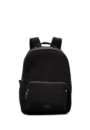 Zaino nero realizzato in tessuto resistente, dotato di una tasca frontale con zip e spallacci regolabili. Design semplice con dettagli in cucitura bianca.