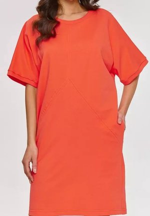 Vrouw draagt een losse, feloranje jurk tot op de knie met korte mouwen, een ronde halslijn en subtiele diagonale naaddetails.