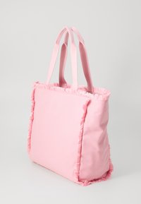 Roze draagtas gemaakt van zacht stof met rafelige accenten langs de randen. Voorzien van twee stevige handvatten en een rechthoekige vorm.