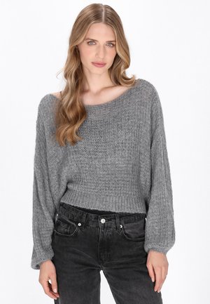 Grauer Strickpullover mit lockerer Passform, weitem Ausschnitt und geripptem Design, kombiniert mit schwarzen Jeans mit dezenten Used-Effekten.
