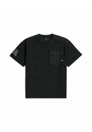 T-shirt noir à manches courtes avec une poche poitrine à boutons et un texte blanc sur la manche gauche.