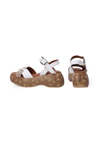 Weiße Plattform-Sandalen mit einer geometrisch braun gemusterten Sohle, ausgestattet mit Kreuzriemen und einer Schnalle am Knöchelriemen für einen sicheren Sitz.