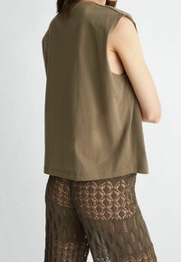 Olivově zelený top bez rukávů vyrobený z měkké látky s volným střihem. Má jednoduchý design bez vzorů nebo kovových prvků.