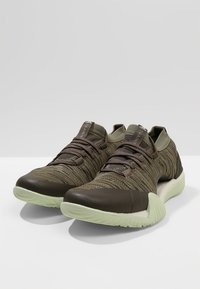 Scarpe sportive con una tomaia in maglia verde oliva testurizzata, punta in pelle marrone e suola in gomma verde chiaro. Presentano un design con lacci.