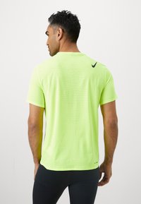 Neon żółta koszulka sportowa, krótki rękaw, teksturowany materiał siatkowy z małymi perforacjami, z czarnym logo Nike w okolicy szyi.