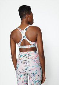 Sutiã desportivo multicolorido com um design de costas nadadora, apresentando um padrão floral em tons pastéis suaves, combinado com leggings de cintura alta a condizer.