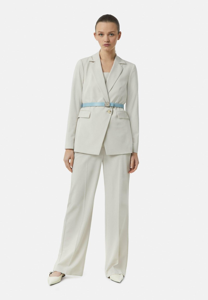 White blazer with structured shoulders and two front pockets, paired with wide-leg trousers and a light blue belt accentuating the waist.