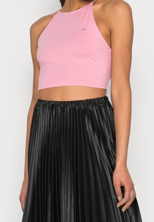 Kvinde iført en pink ærmeløs cropped top og et sort plisseret nederdel i høj talje med blankt materiale.