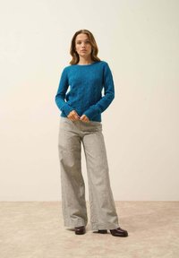 Teal kabelstickad tröja med ribbade muddar, matchad med ljusgrå vida byxor. Modellen bär mörk burgunder plattformsskor.