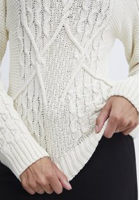 Gebreide trui in off-white, met gestructureerde kabelpatronen, brede ribgebreide manchetten en een V-vormige zoom. Zachte, ademende stof.
