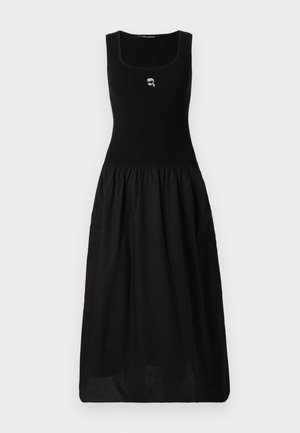 Robe noire avec un haut ajusté en côtes et une jupe fluide et froncée. Les détails incluent un petit emblème sur la poitrine et une couleur unie dans l'ensemble.