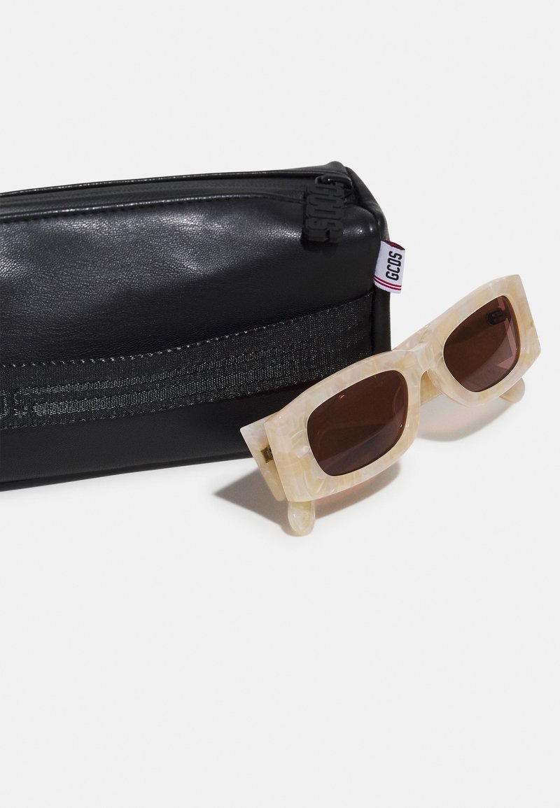 Sunglasses with a marbled beige frame, dark brown lenses, placed next to a matte black zippered case with a visible logo and strap.