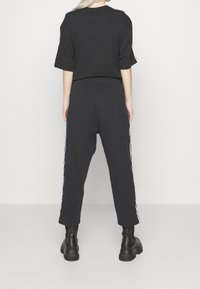 Černé bavlněné tričko s krátkým ruk ávem, kombinované s černými tepláky s bílými bočními pruhy. Celkový uvolněný střih, texturovaná tkanina.