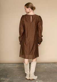 Brun kjole med prikker og puffede ærmer samt en nøglehul-lukning bagpå. Stylet med knæhøje beige ruskinds westernstøvler. Glat tekstur.