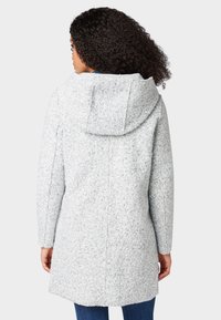 Šedý, strukturovaný kabát s kapucí, s rovnými liniemi a dlouhými rukávy, viditelnými švy a délkou do poloviny stehna.