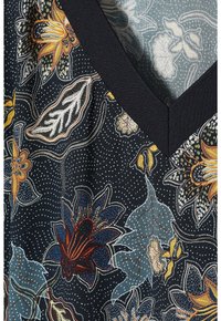 Blusa floral con un fondo negro y patrones de flores y hojas coloridas. Escote en V con ribete negro sólido, fabricada en tela ligera.