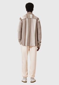 Gestreepte bruine gebreide shirt met een relaxte pasvorm, voorzien van een klassieke kraag en rafelige randen, gecombineerd met lichtbeige sweatpants en grijze schoenen.