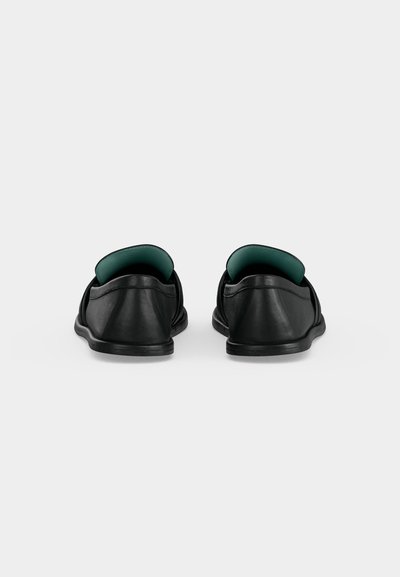 Ζευγάρι μαύρα παπούτσια slip-on με χαμηλά τακούνια, εμφανιζόμενα από πίσω σε απλό λευκό φόντο.