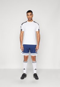 Vit sporttröja med svarta ränder på axlarna, i kombination med blå shorts med vita detaljer. Svarta skor och knälånga vita strumpor.