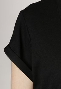 Svart kortärmad topp med uppvikt ärm, med en mjuk textur och en enkel, ren design. Tyget verkar flexibelt och slätt.