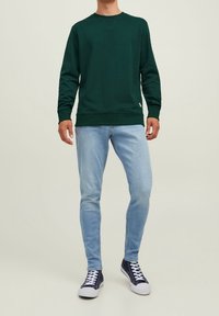 Felpa verde con maniche lunghe e collo rotondo, abbinata a jeans azzurri chiari e sneakers navy. Design semplice, materiale in cotone.