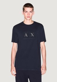 T-shirt bleu marine à manches courtes en coton avec un col rond, présentant un graphique du logo "AX" et le texte "Armani Exchange" sur le devant.
