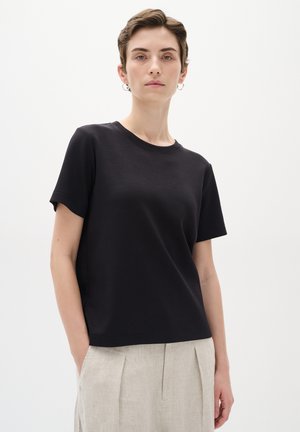 T-shirt nera a maniche corte in tessuto morbido con scollo rotondo e vestibilità rilassata, abbinata a pantaloni beige chiaro larghi.
