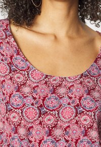 Červená a modrá látka s vzorem obsahujícím kruhové motivy a výstřih do lodičky. Měkká struktura s propracovanými designy po celém povrchu.