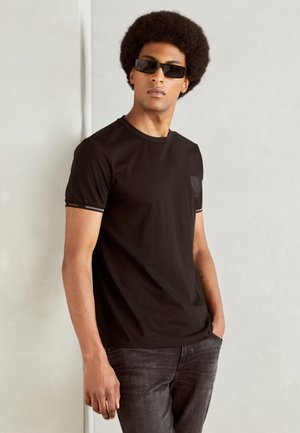 Camiseta de algodón negra con mangas cortas, que presenta un logo sutil en el pecho y un ribete en contraste alrededor del escote y las mangas.