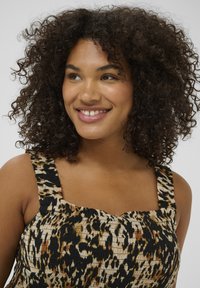 Haut à imprimé animal avec de larges bretelles, présentant une texture smockée en noir, beige et marron, porté par un modèle aux cheveux bouclés.
