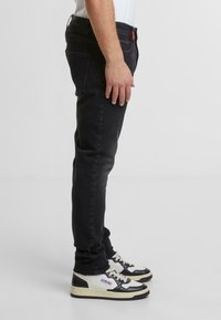 Jeans negros ajustados con una textura suave, pasadores para cinturón y costuras rojas en contraste. Combinados con zapatillas de estilo retro en blanco y negro.