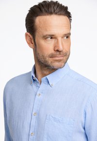 Lichtblauw overhemd van een linnenmix met een borstzak, voorzien van een puntkraag en subtiele textuur. De knopen zijn metallic.