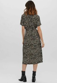 Tigermönstrad midiklänning i ett lätt tyg, med korta ärmar och en samlad snörning vid midjan. Svarta ankelskor fulländar looken.