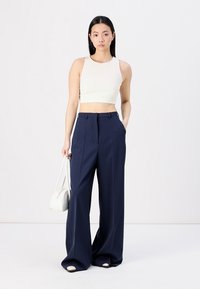 Top cropped creme e calças largas azul-marinho, com cintura alta e textura suave. Combinado com uma pequena bolsa branca.
