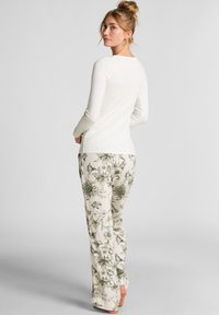 Witte lange mouwen top gecombineerd met crèmekleurige pyjamabroek met groene bloemenpatronen en zachte texturen, gezien vanuit de rug.