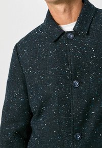 Svart skjortjacka i herringbone-mönster med flerfärgade prickar, spetskrage och blå knappar. Mjuk textur och skräddarsydd passform.