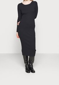 Vestido midi negro con relieve, de mangas largas y escote en forma de barco, combinado con botas negras texturizadas hasta la rodilla. Textura de tela suave.