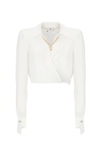 Blusa bianca a maniche lunghe, corta, realizzata in un tessuto liscio con un design avvolgente. Presenta una collana in catena dorata e accenti con bottoni a contrasto.