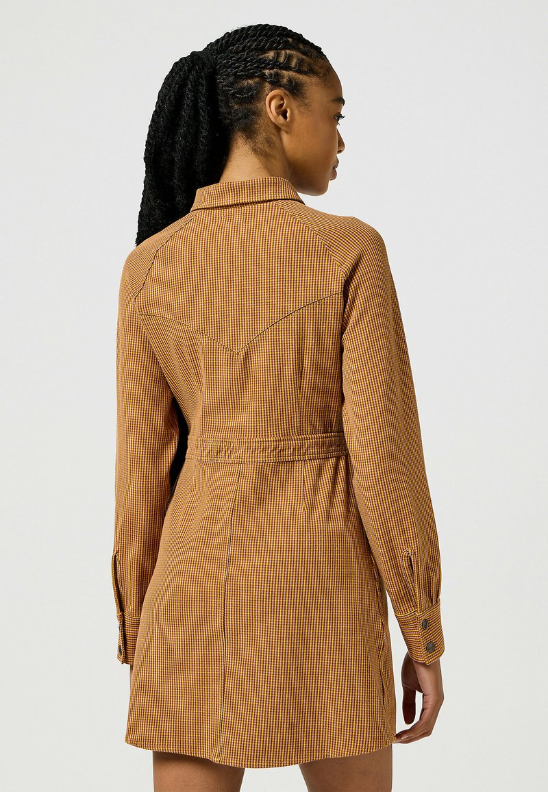 Robe a maniche lunghe a quadri in tonalità arancioni e gialle. Presenta un colletto, una vita cintrata e polsini con bottoni. Tessuto morbido.