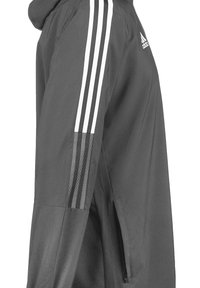 Graue Jacke mit drei weißen Streifen entlang der Schulter, einem strukturierten Akzent und einer Reißverschlusstasche an der Seite.