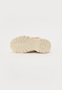 Suela de una zapatilla con un material de goma texturizado en color beige, con surcos pronunciados y un logo circular en el talón.