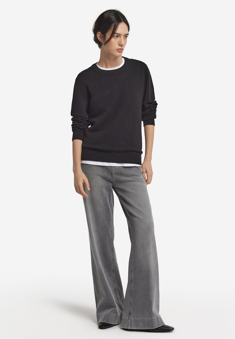 Czarna bluza z okrągłym dekoltem, długimi rękawami i ściągaczami. W połączeniu z szarymi dżinsami o szerokich nogawkach i czarnymi butami z noskiem w szpic.