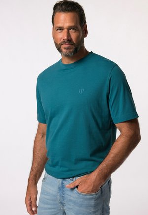 Camiseta corta de manga corta en color azul verde con un cuello redondo y un logotipo sutil en el pecho. Tejido suave, corte relajado, combinada con jeans azul claro.