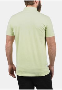 Lichtgroen poloshirt met korte mouwen, gemaakt van zachte stof. Bevat een kraag en een klein label aan de linksonderkant. Eenvoudig, getailleerd ontwerp.
