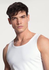 White cotton tank top with a round neckline and wide shoulder straps, featuring a smooth texture and fitted design.