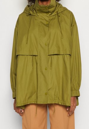 Olive green oversized jacket with button closure, drawstrings at hood and hem, worn over tan pants.