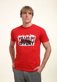 Rød bomulds t-shirt med "MAXIMUM EFFORT" grafik i fed sort og hvid. Korte ærmer og rund halsudskæring, simpel design uden detaljer.