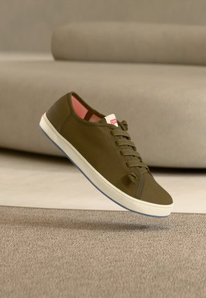 Olivgrüner Sneaker mit einem strukturierten Stoffoberteil, weißer Gummisohle und rosa Innenfutter. Verfügt über fünf Ösen und ein kleines Logetikett.